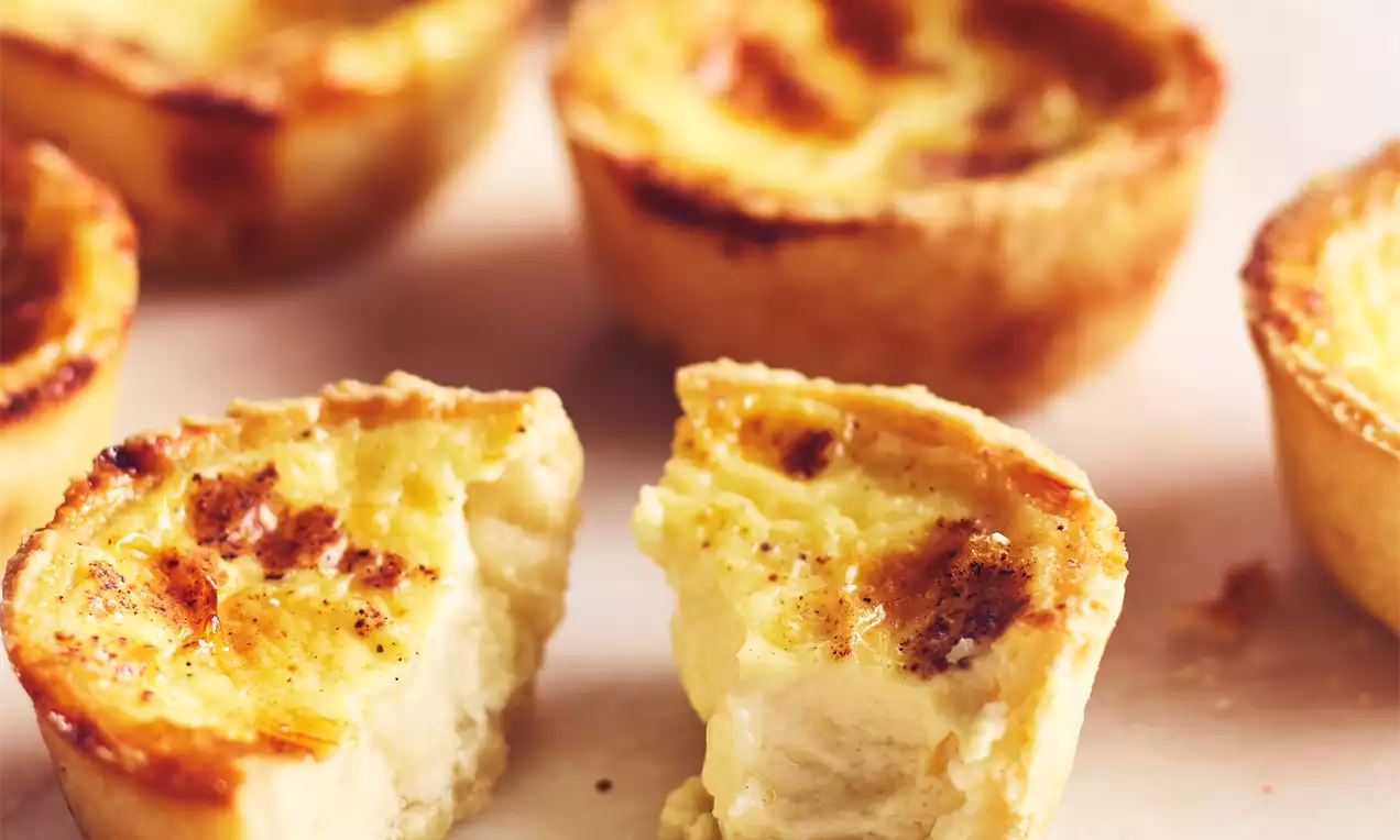 Tartelettes dorées à la crème jaune onctueuse avec une pâte croustillante et des bords délicatement caramélisés sur papier cuisson