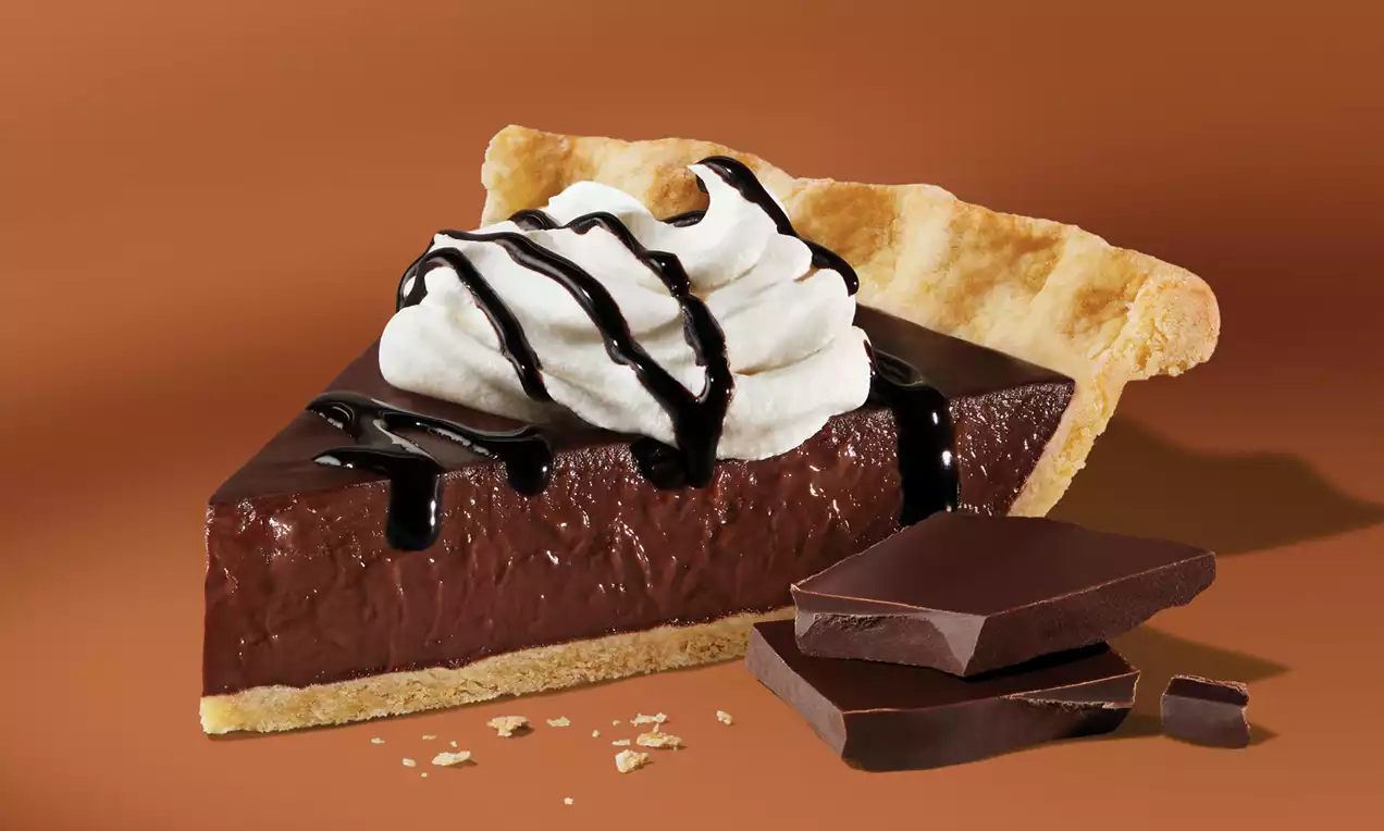 Part de tarte au chocolat brillante sur pâte dorée, garnie de crème légère et d'un filet de chocolat noir avec éclats de chocolat à côté
