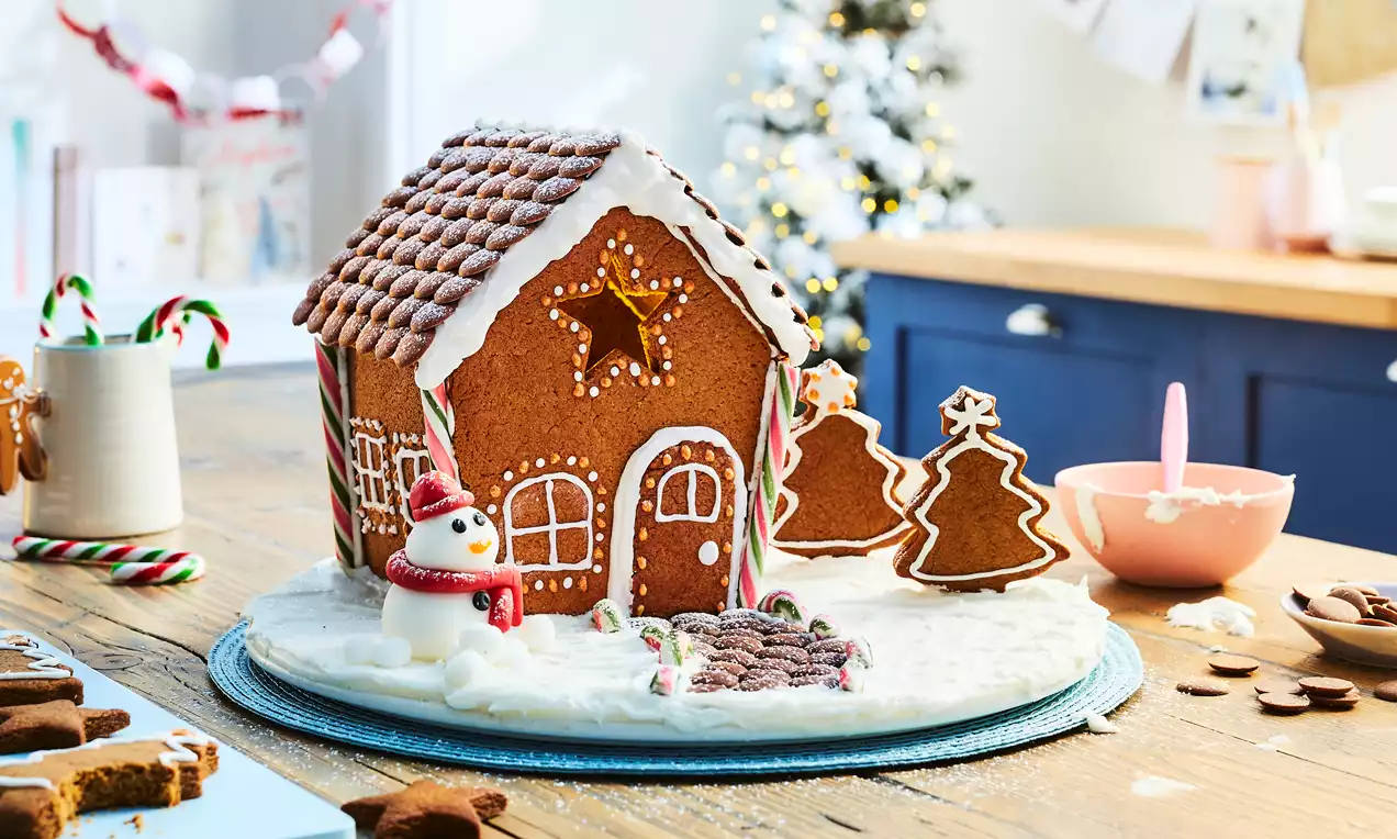 Maison en pain d’épices brun ornée de glaçage blanc, décorée de bonbons rouges et cannes en sucre sur un tapis de neige en sucre