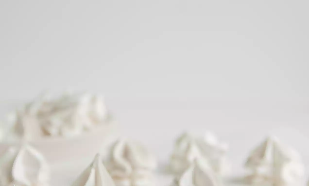 Small swirls of vegan whipped cream bright white and silky smooth with peaked tops arranged on a white surface