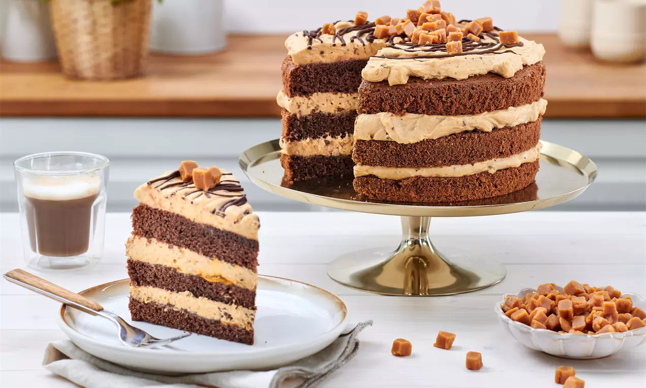 Gâteau à étages avec génoise chocolat moelleuse et crème caramel, garni de cubes de caramel et filet de chocolat sur un plat doré